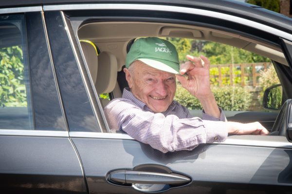 A man leans out of the window of his car and tips his hat