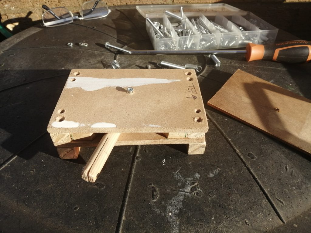 Work bench with wooden prototype of guitar strummer, along with work tools and a pair of glasses