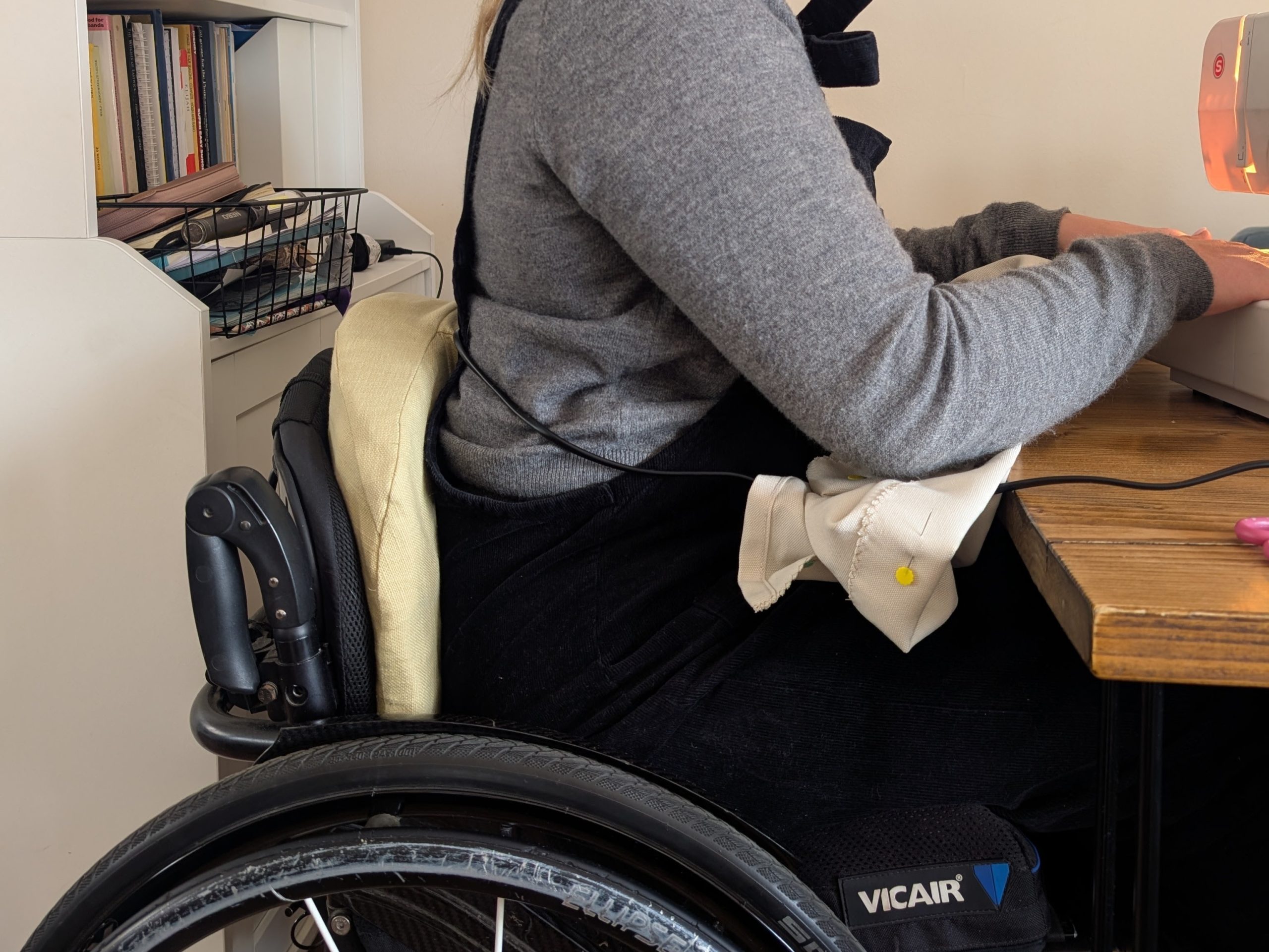 Person using sewing machine by pressing cushion in wheelchair